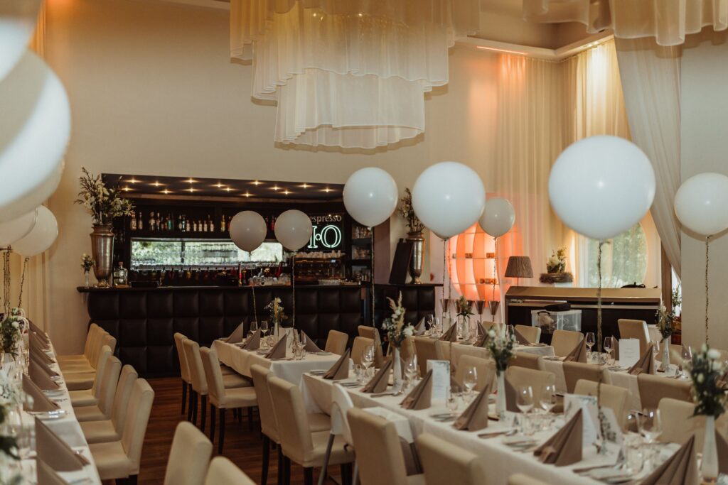 Sala weselna, za białymi balonami i nakrytymi stołami.